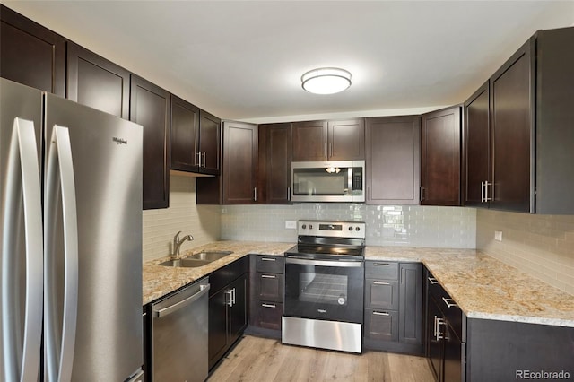 kitchen with dark brown cabinetry, sink, light hardwood / wood-style flooring, stainless steel appliances, and light stone countertops