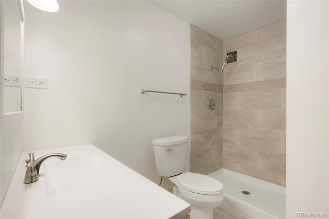 bathroom featuring tiled shower, toilet, and sink