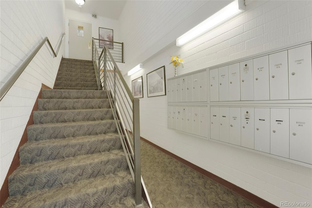 stairway with brick wall, carpet flooring, and a mail area