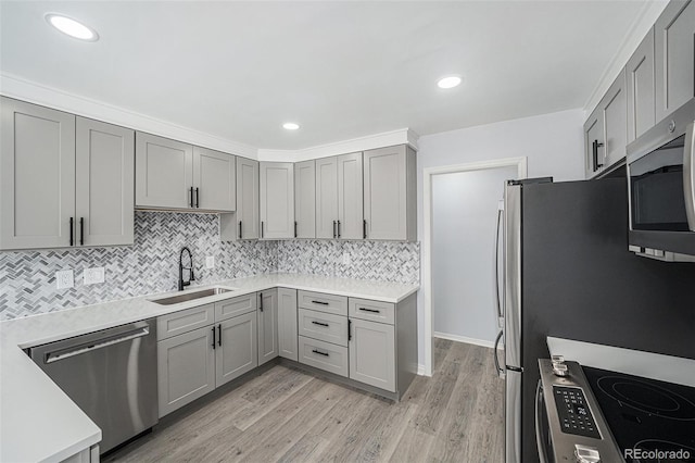 kitchen with light wood-style flooring, gray cabinets, stainless steel appliances, light countertops, and a sink