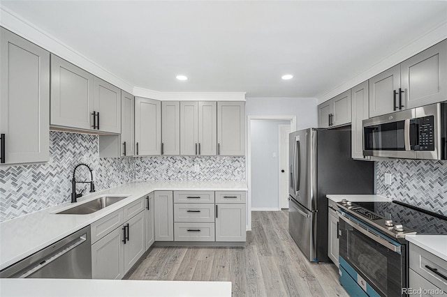 kitchen with stainless steel appliances, a sink, light countertops, gray cabinets, and light wood finished floors