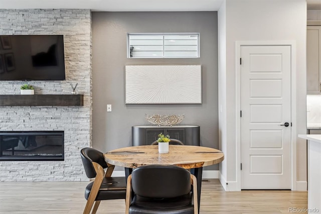dining space with light wood-style flooring, baseboards, and a fireplace