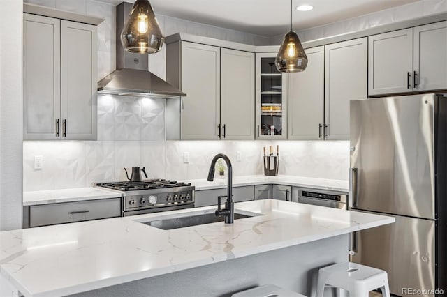 kitchen with a sink, wall chimney range hood, stainless steel appliances, decorative backsplash, and light stone counters