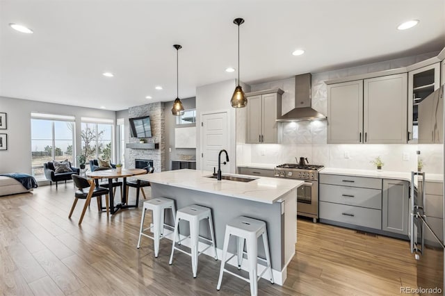 kitchen featuring wall chimney exhaust hood, stainless steel stove, a sink, open floor plan, and gray cabinetry