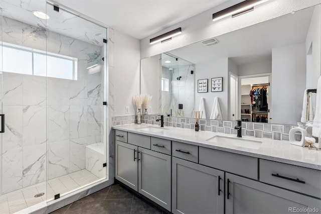 bathroom featuring double vanity, a marble finish shower, a sink, and backsplash