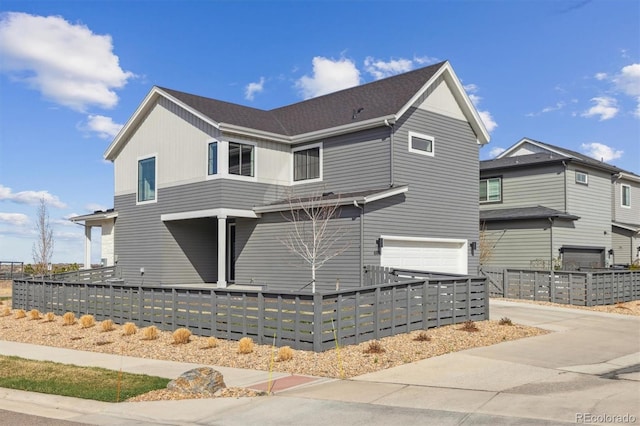 view of side of home featuring concrete driveway, an attached garage, and a fenced front yard