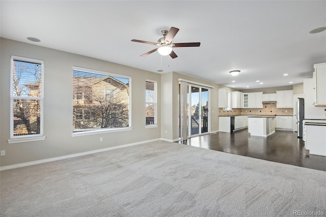 unfurnished living room featuring ceiling fan and dark colored carpet