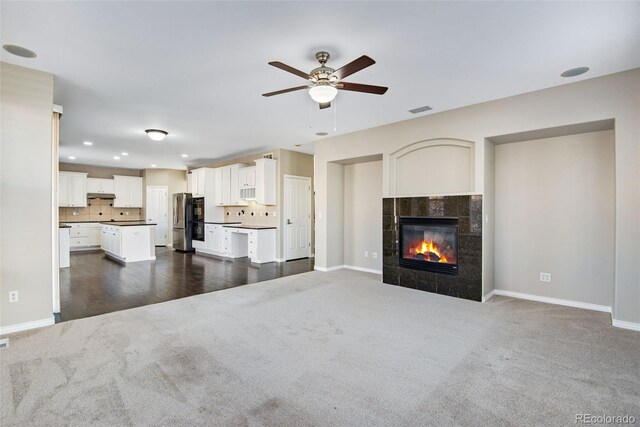 unfurnished living room with a fireplace, dark colored carpet, and ceiling fan