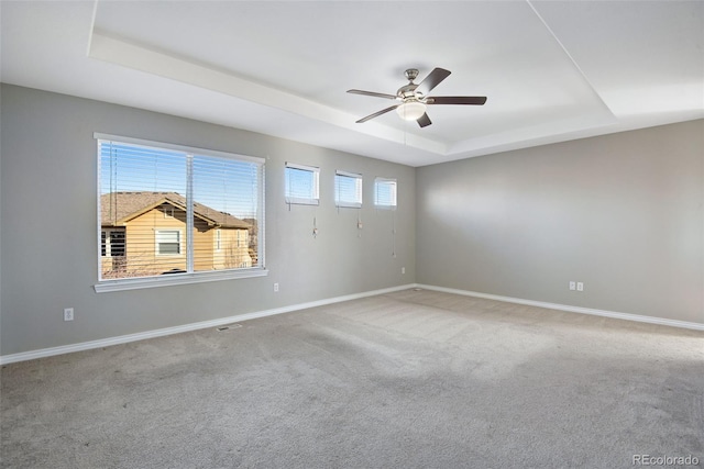 empty room with carpet floors, a raised ceiling, a wealth of natural light, and ceiling fan