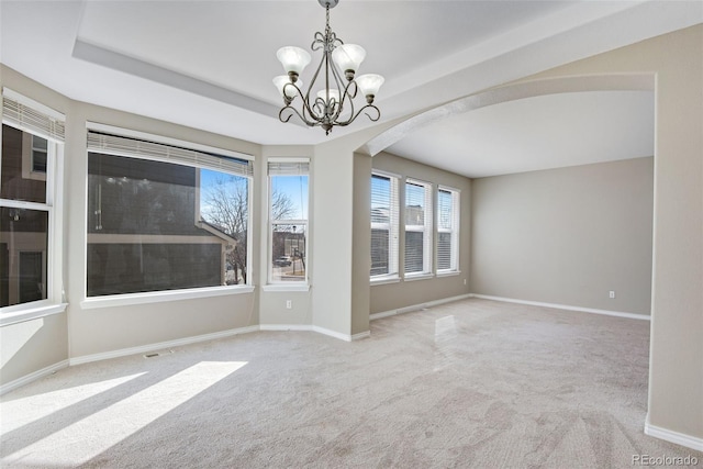 empty room with a raised ceiling, light carpet, and a chandelier