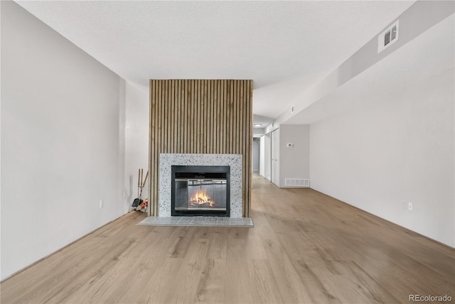 unfurnished living room with a textured ceiling, light wood-style flooring, a glass covered fireplace, and visible vents