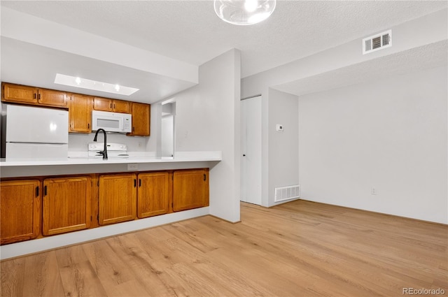 kitchen featuring brown cabinetry, light countertops, white appliances, and visible vents