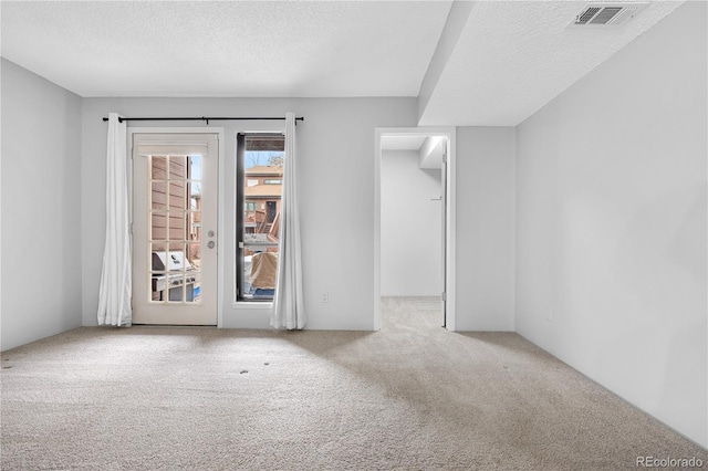 spare room with light carpet, visible vents, and a textured ceiling