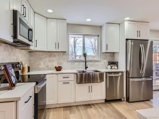 kitchen with stainless steel appliances, light wood-type flooring, sink, white cabinetry, and backsplash