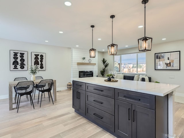 kitchen featuring a fireplace, a center island, light wood-type flooring, light stone countertops, and pendant lighting