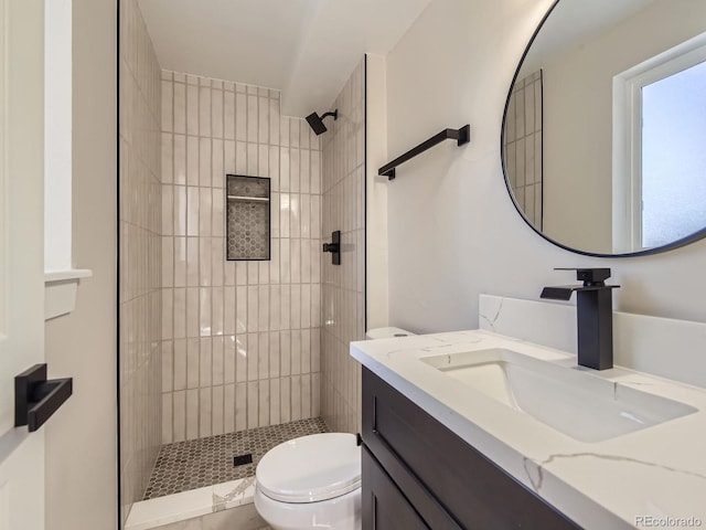 bathroom with tiled shower, vanity, and toilet