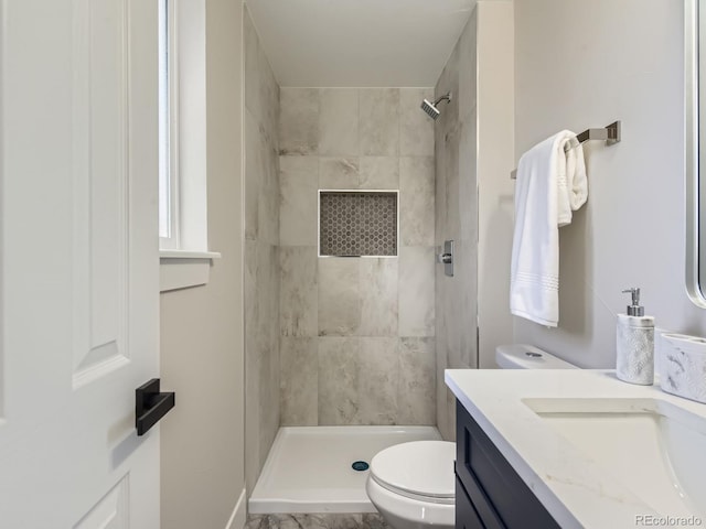 bathroom featuring toilet, tiled shower, and vanity