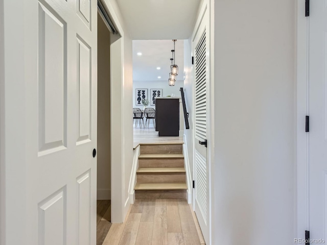 corridor with light wood-type flooring and a notable chandelier