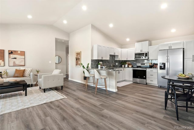 kitchen featuring kitchen peninsula, a kitchen bar, white cabinetry, stainless steel appliances, and high vaulted ceiling