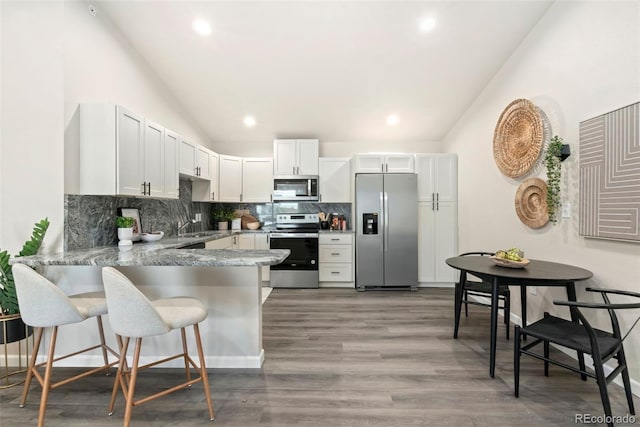 kitchen with white cabinetry, kitchen peninsula, a breakfast bar area, appliances with stainless steel finishes, and dark wood-type flooring