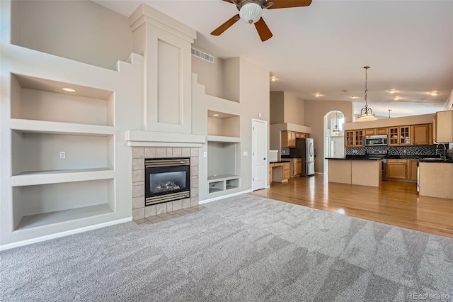 22436 E Maplewood Pl, Aurora, CO 80015 - unfurnished living room featuring light colored carpet, built in features, ceiling fan, a tiled fireplace, and a high ceiling