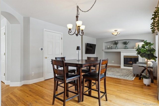 dining room with a notable chandelier, built in shelves, and light hardwood / wood-style flooring