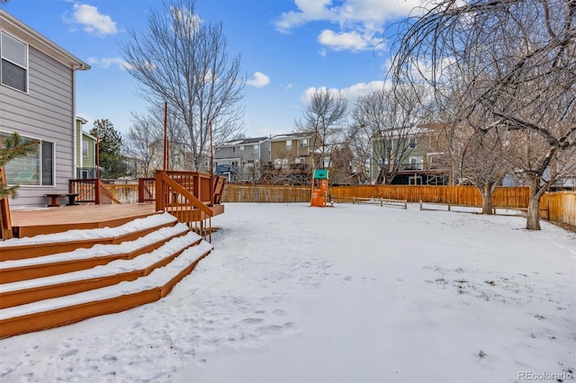 snowy yard featuring a playground and a deck