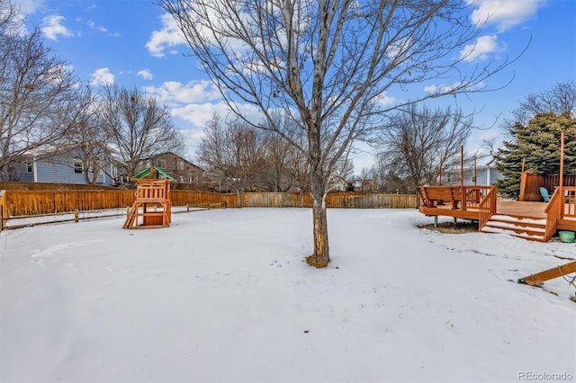 yard layered in snow featuring a playground and a deck