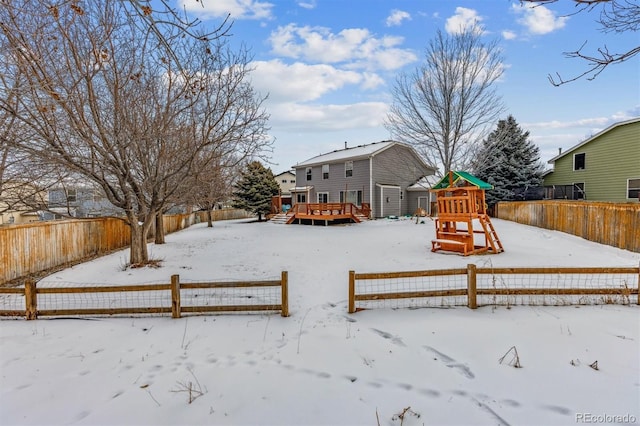 yard covered in snow featuring a playground and a wooden deck