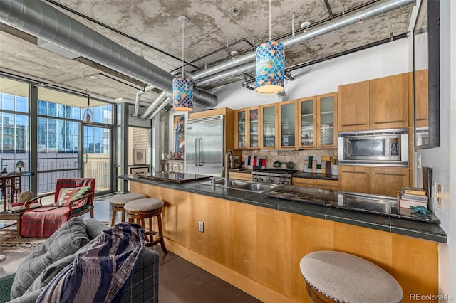 kitchen with built in appliances, a breakfast bar, a sink, brown cabinets, and dark countertops