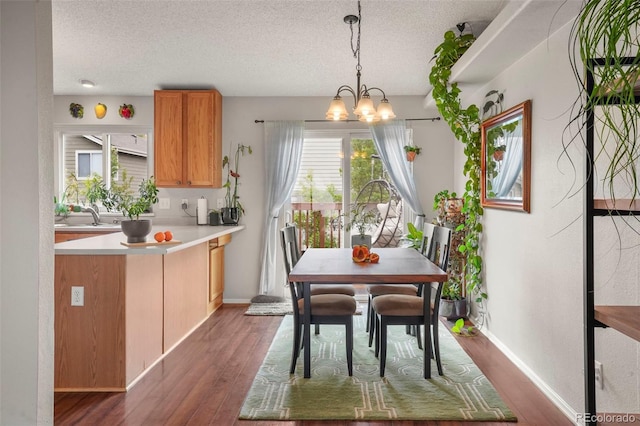 dining area featuring a textured ceiling, dark wood-style flooring, a chandelier, and baseboards