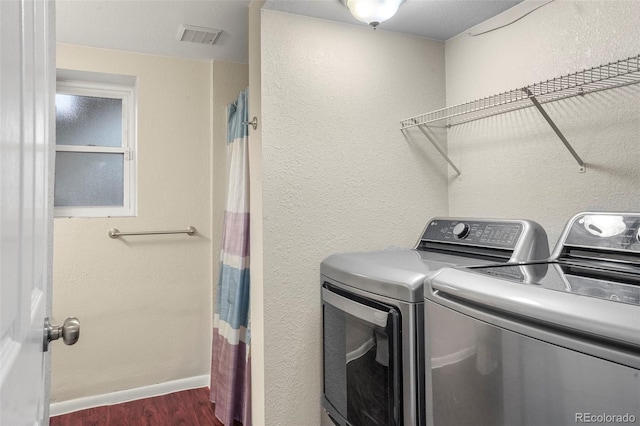 clothes washing area with washer and clothes dryer, dark wood-type flooring, a textured wall, and baseboards