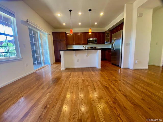 kitchen featuring appliances with stainless steel finishes, light hardwood / wood-style floors, pendant lighting, and a breakfast bar area