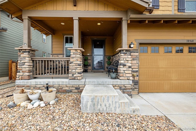 doorway to property with covered porch, stone siding, and an attached garage