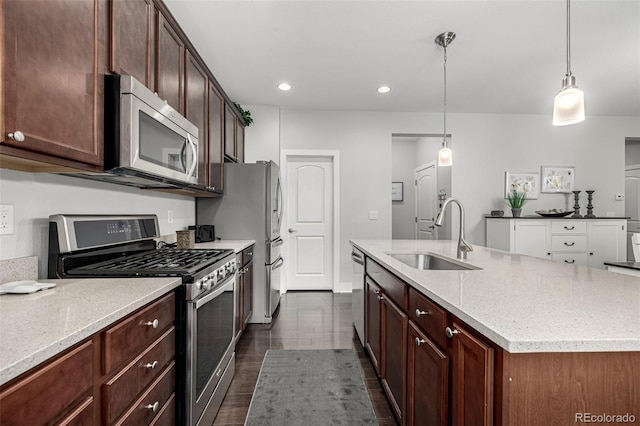 kitchen with light stone counters, hanging light fixtures, appliances with stainless steel finishes, a sink, and an island with sink