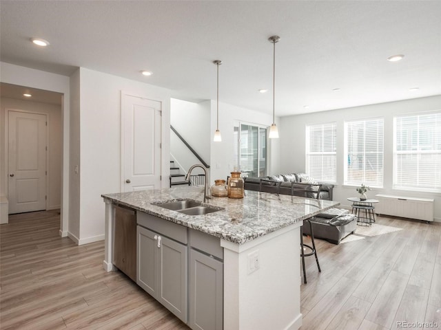 kitchen with stainless steel dishwasher, light hardwood / wood-style flooring, an island with sink, and sink