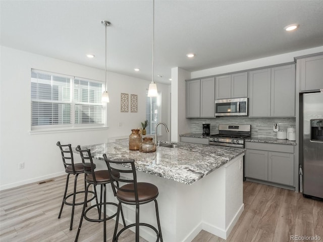 kitchen featuring sink, stainless steel appliances, a center island with sink, and light hardwood / wood-style flooring