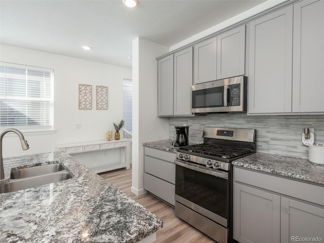 kitchen with light wood-type flooring, stainless steel appliances, sink, decorative backsplash, and stone countertops