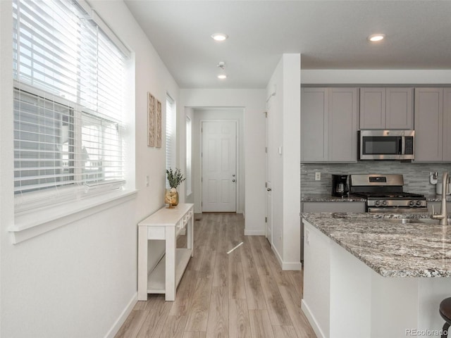 kitchen with gray cabinetry, appliances with stainless steel finishes, light stone counters, light hardwood / wood-style floors, and decorative backsplash