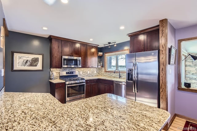 kitchen with stainless steel appliances, tasteful backsplash, light stone countertops, light hardwood / wood-style floors, and kitchen peninsula