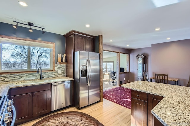 kitchen with sink, stainless steel appliances, light stone counters, light hardwood / wood-style floors, and decorative backsplash