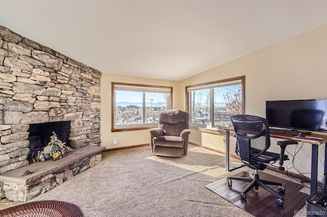 carpeted office featuring a stone fireplace and vaulted ceiling