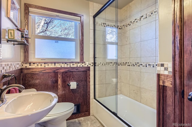 full bathroom featuring combined bath / shower with glass door, sink, tile walls, and toilet