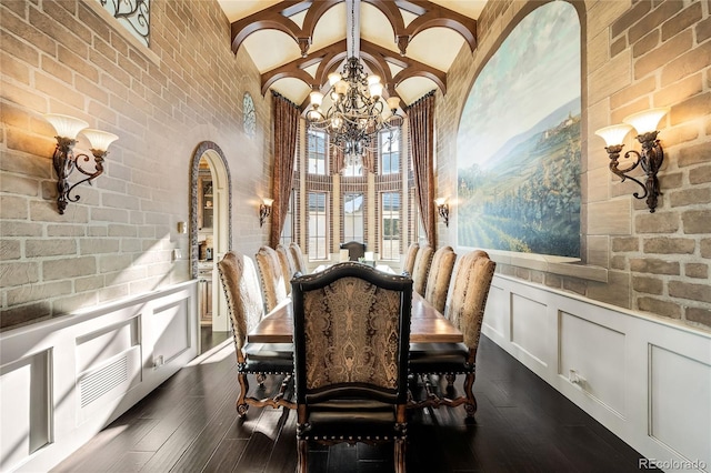 dining room featuring beamed ceiling, brick wall, dark wood-type flooring, and a notable chandelier