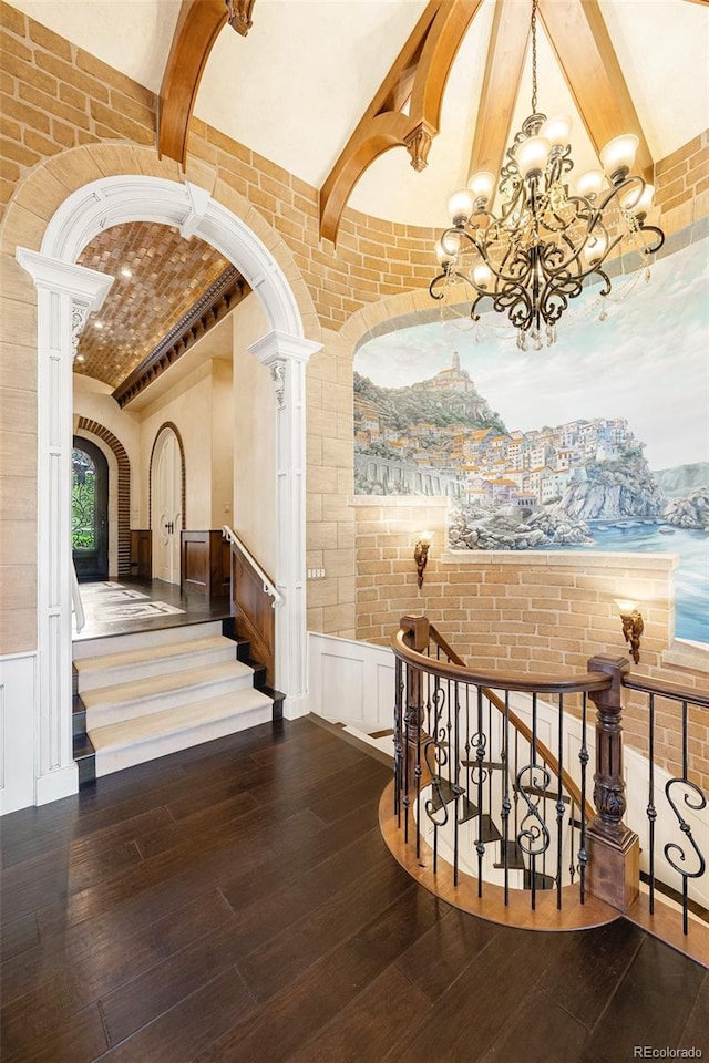 7188 Raphael Ln, Littleton, CO 80125 - stairs featuring brick ceiling, wood-type flooring, a chandelier, brick wall, and decorative columns