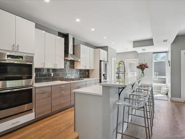 2508 S Pennsylvania St, Denver, CO 80210 - kitchen featuring appliances with stainless steel finishes, wall chimney exhaust hood, light wood-style floors, a kitchen bar, and backsplash
