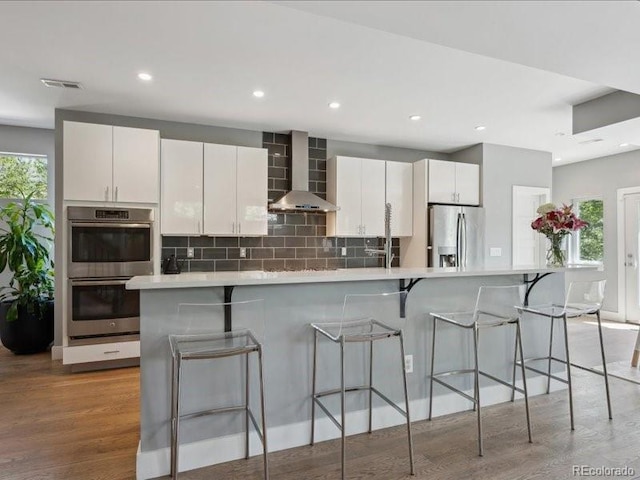 2508 S Pennsylvania St, Denver, CO 80210 - kitchen with stainless steel appliances, wall chimney exhaust hood, backsplash, white cabinetry, and light countertops
