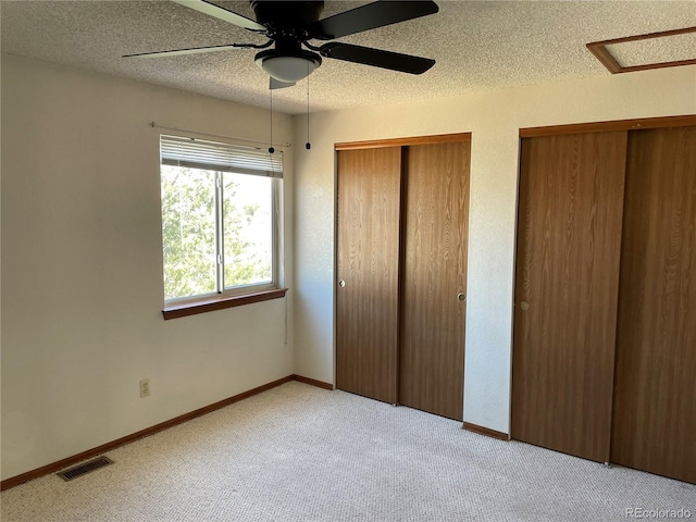 unfurnished bedroom with two closets, a textured ceiling, visible vents, carpet floors, and baseboards