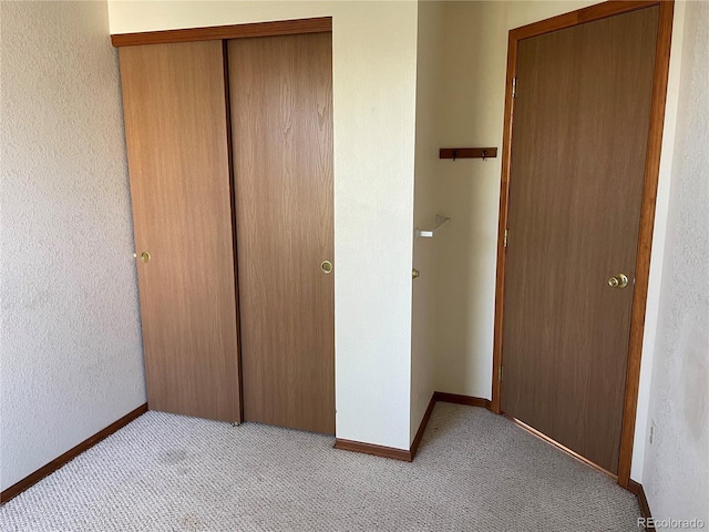 unfurnished bedroom featuring light carpet, a closet, baseboards, and a textured wall