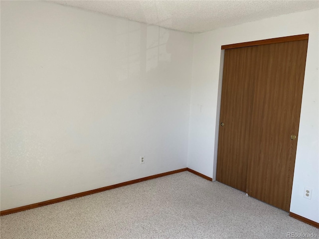 spare room featuring baseboards, light colored carpet, and a textured ceiling